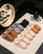 Variety of autumn and winter plush slippers in soft colors displayed on a rug, showcasing cozy indoor comfort.