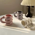 Iridescent pastel ceramic bubble mugs with stacked-ring handles in pink, purple, and white on a table.