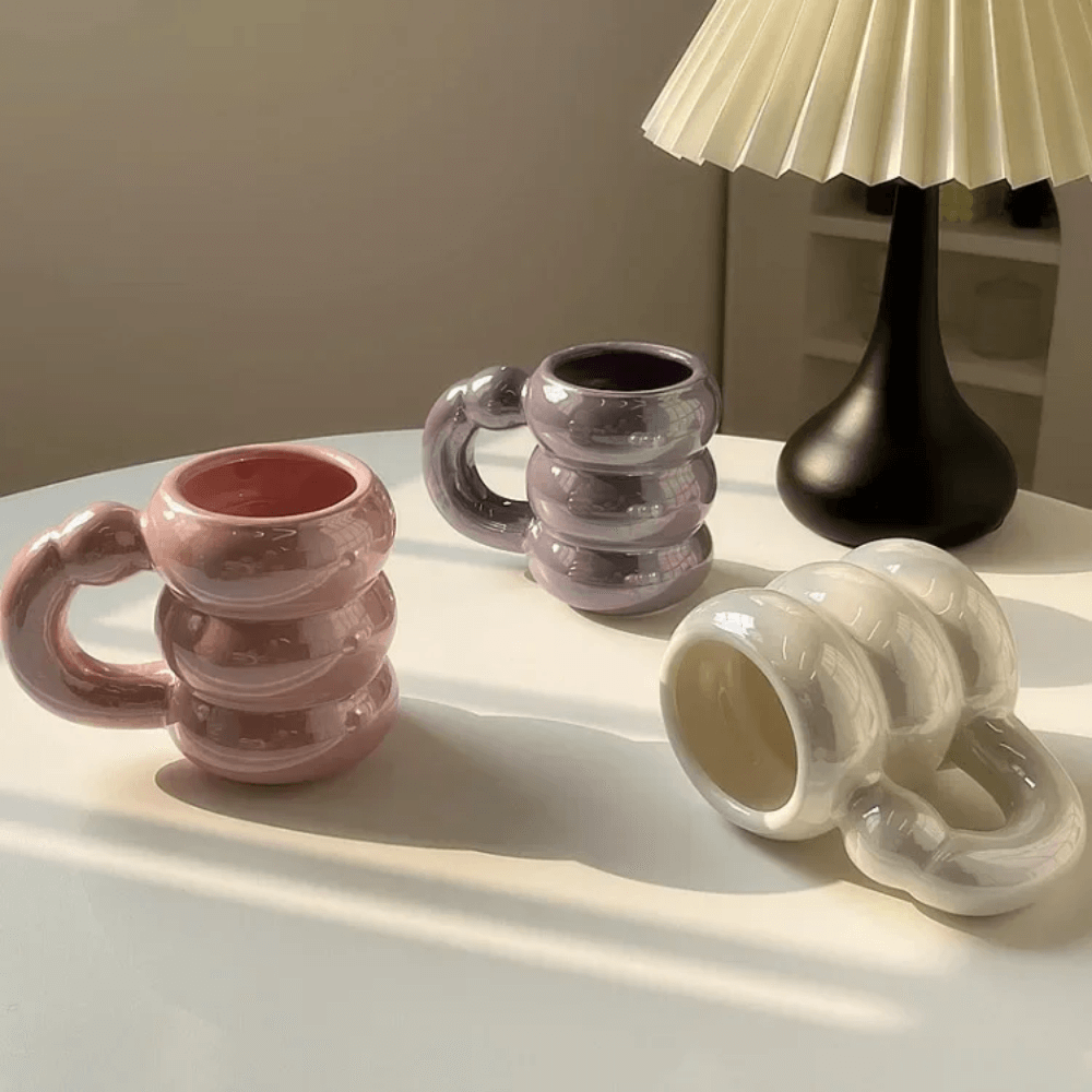 Iridescent pastel ceramic bubble mugs with stacked-ring handles in pink, purple, and white on a table.