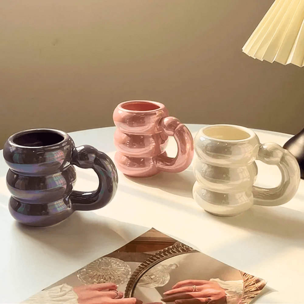 Ceramic Bubble Mugs in iridescent pastel colors with stacked-ring handles on a table, perfect for stylish coffee and tea.