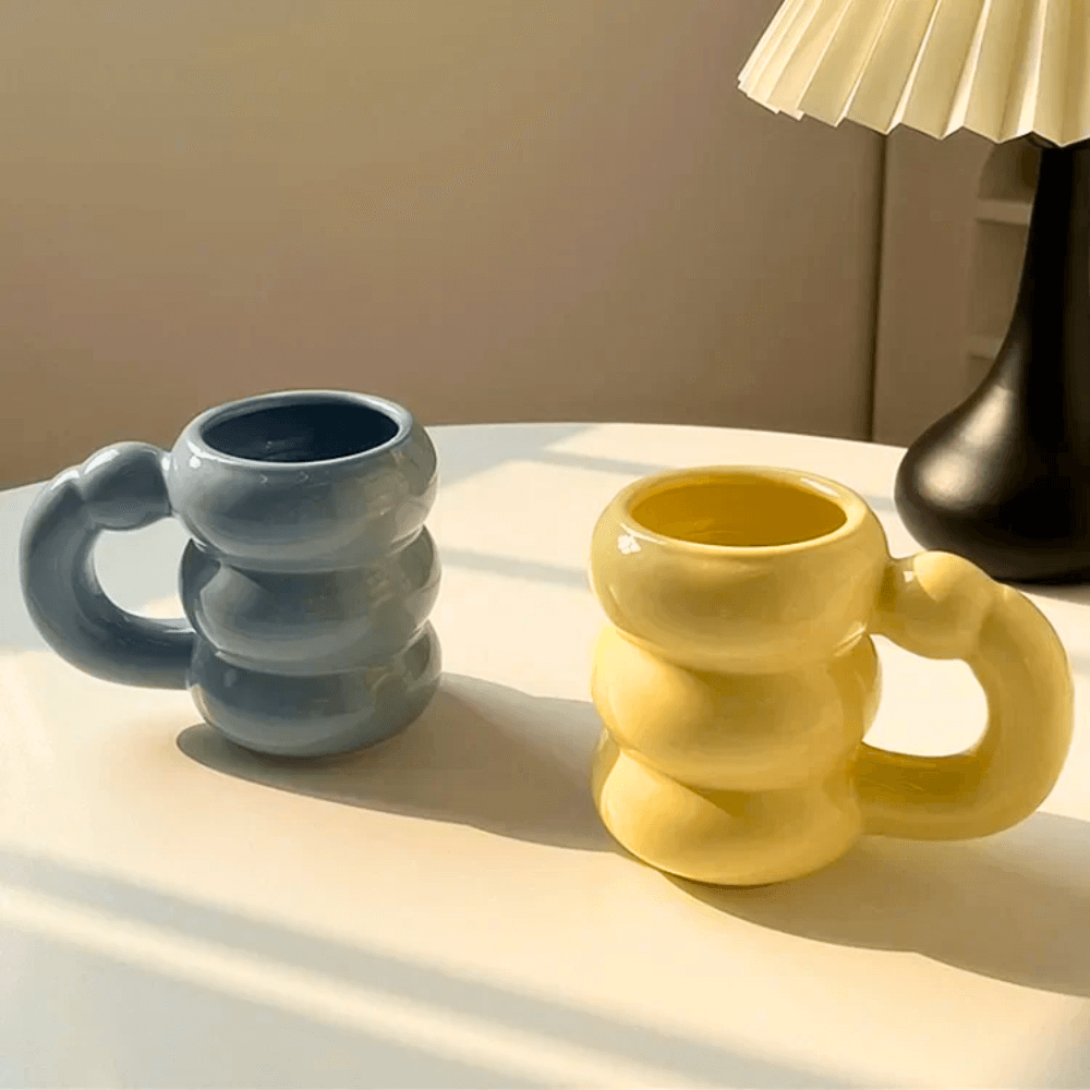 Ceramic bubble mugs in blue and yellow with stacked-ring handles, elegantly displayed on a table.
