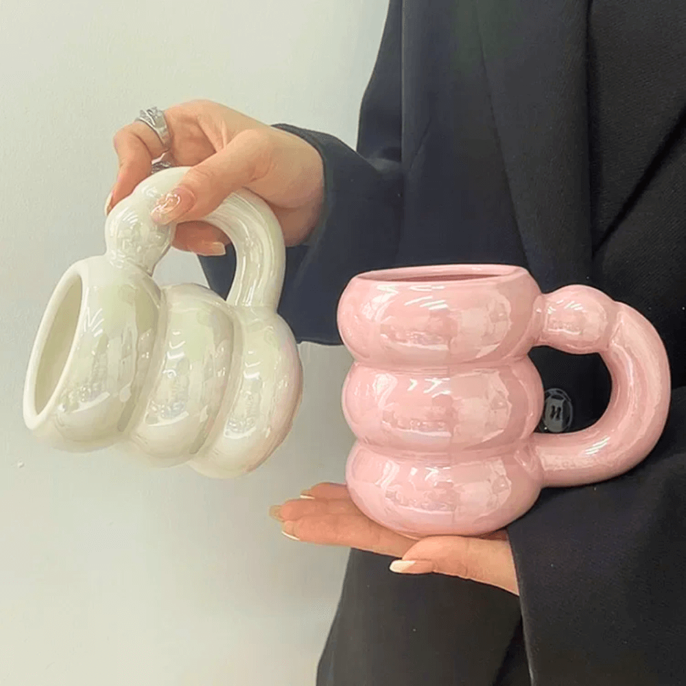 Person holding iridescent pastel ceramic bubble mugs in pink and white with stacked-ring handles.