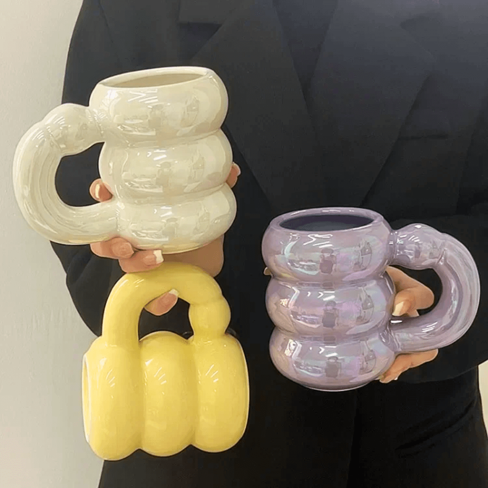 Three iridescent ceramic bubble mugs with stacked-ring handles in pastel colors, held by a person.