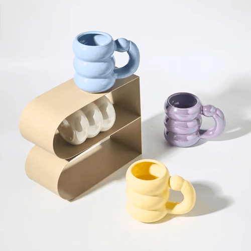 Ceramic bubble mugs in pastel colors stacked on a modern display, showcasing unique handles and glossy finishes.