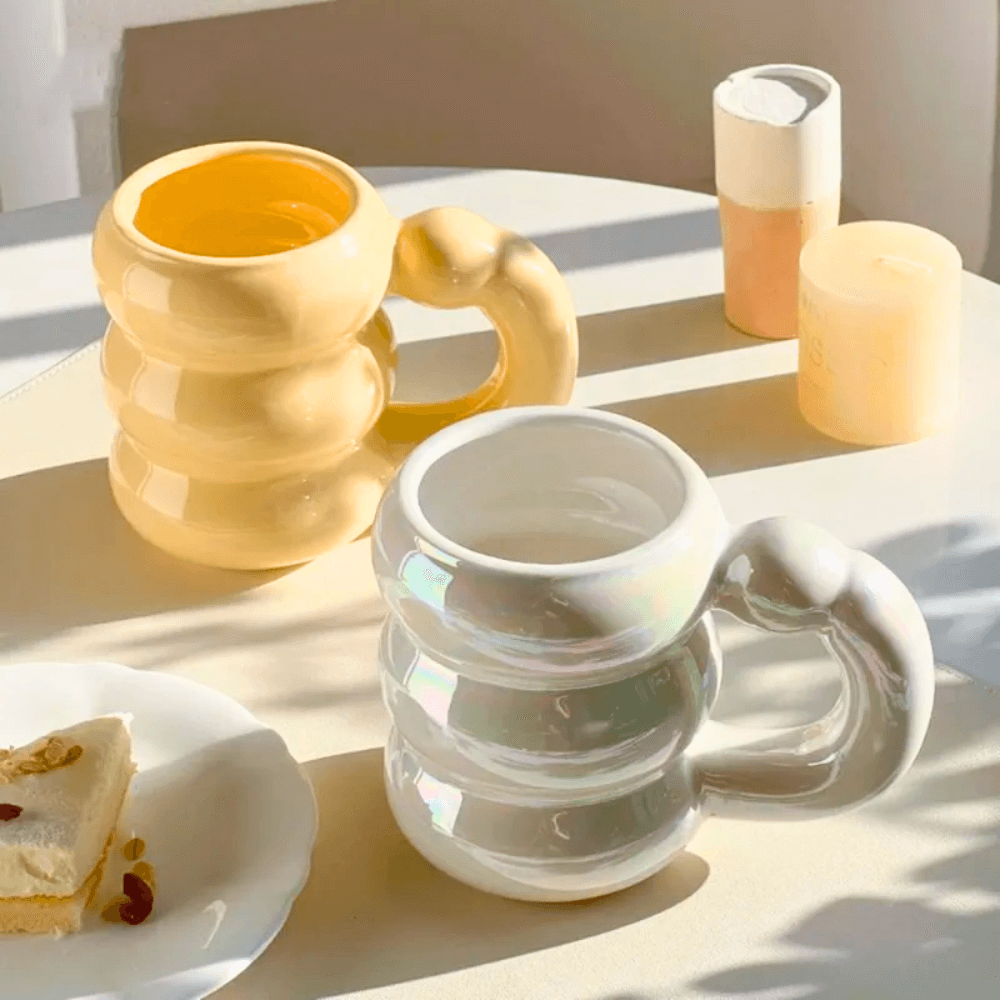 Ceramic bubble mugs in iridescent pastel colors on table with dessert, featuring unique stacked-ring handles.