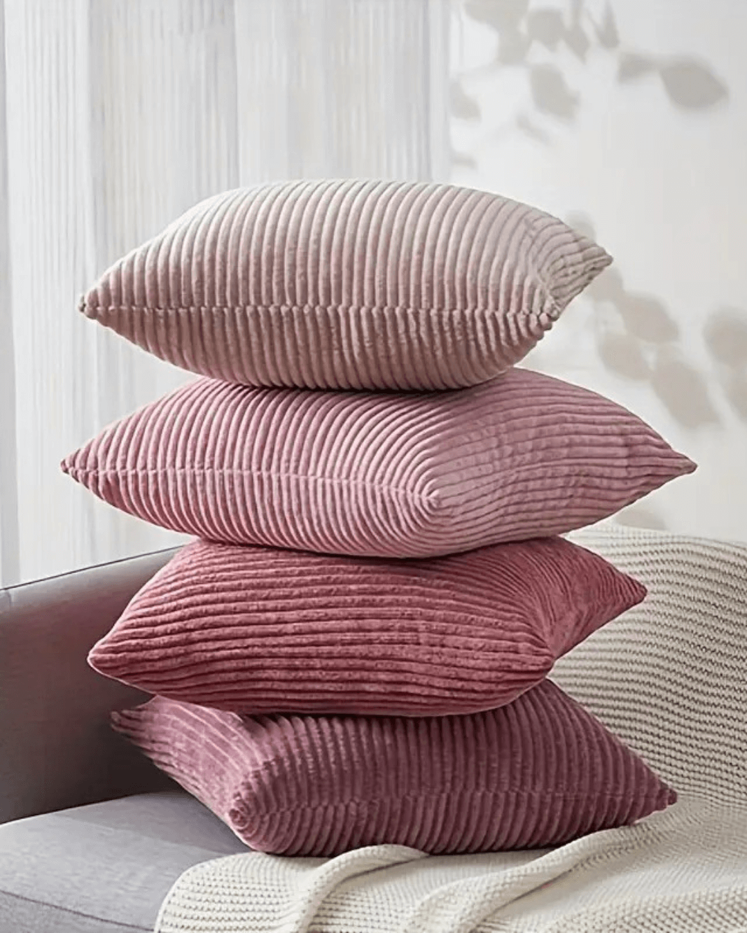Stack of soft pink corduroy decorative pillow covers in boho style on a sofa.