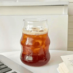 Heat-resistant matcha glass tumbler filled with iced drink on a table beside a laptop and books.