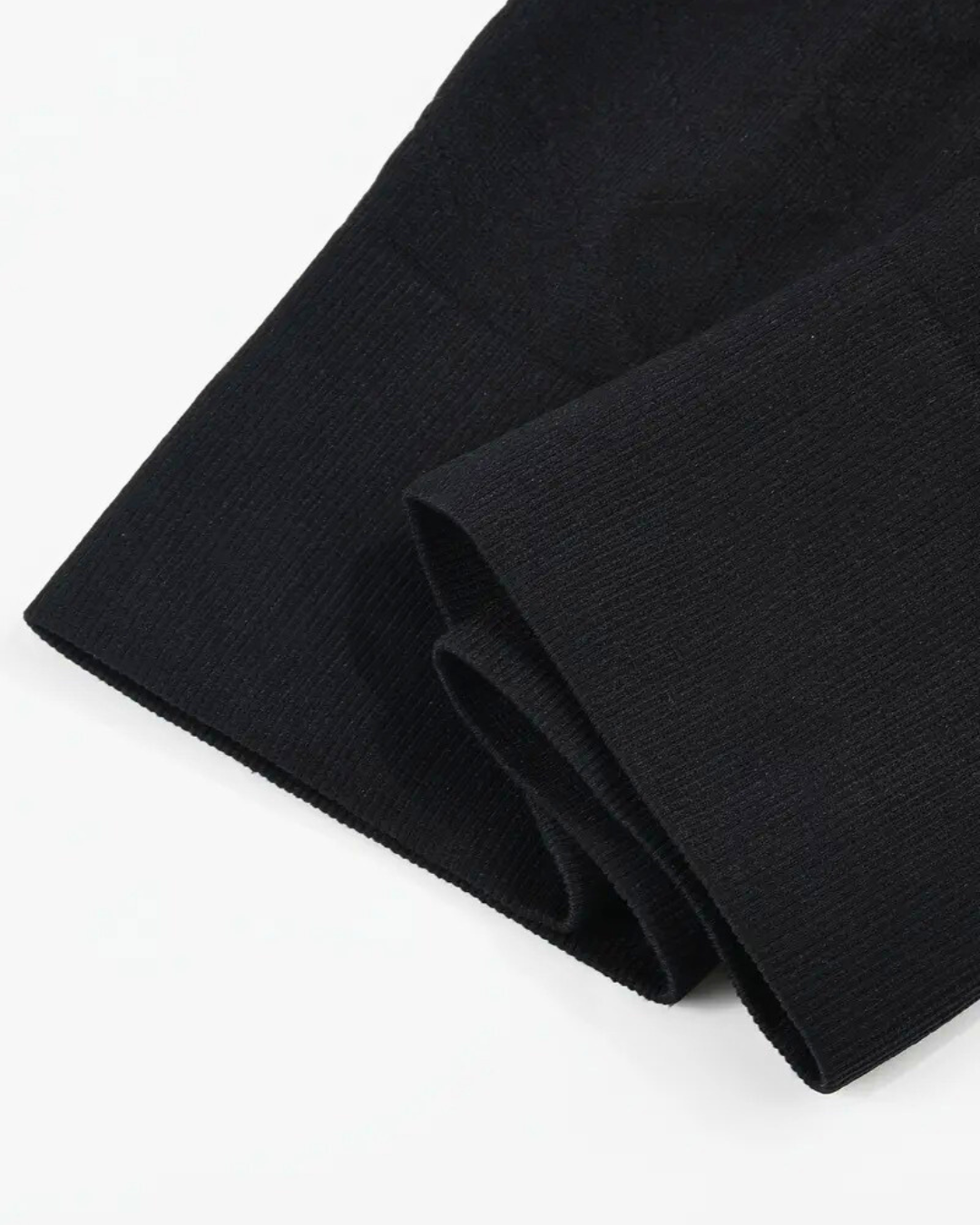 Close-up of the rolled hem of black seamless shapewear shorts, showcasing the high waist and ribbed texture.