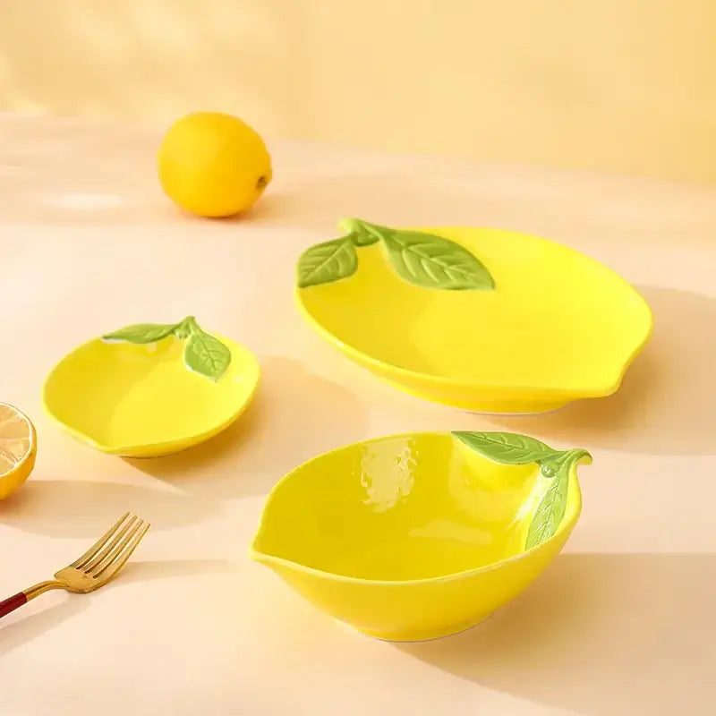 Lemon-shaped ceramic tableware set with yellow plates and bowls featuring green leaf accents.