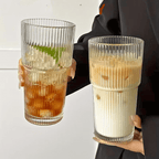 Two ribbed glass tumblers held by a person, one with iced drink and the other with creamy beverage.