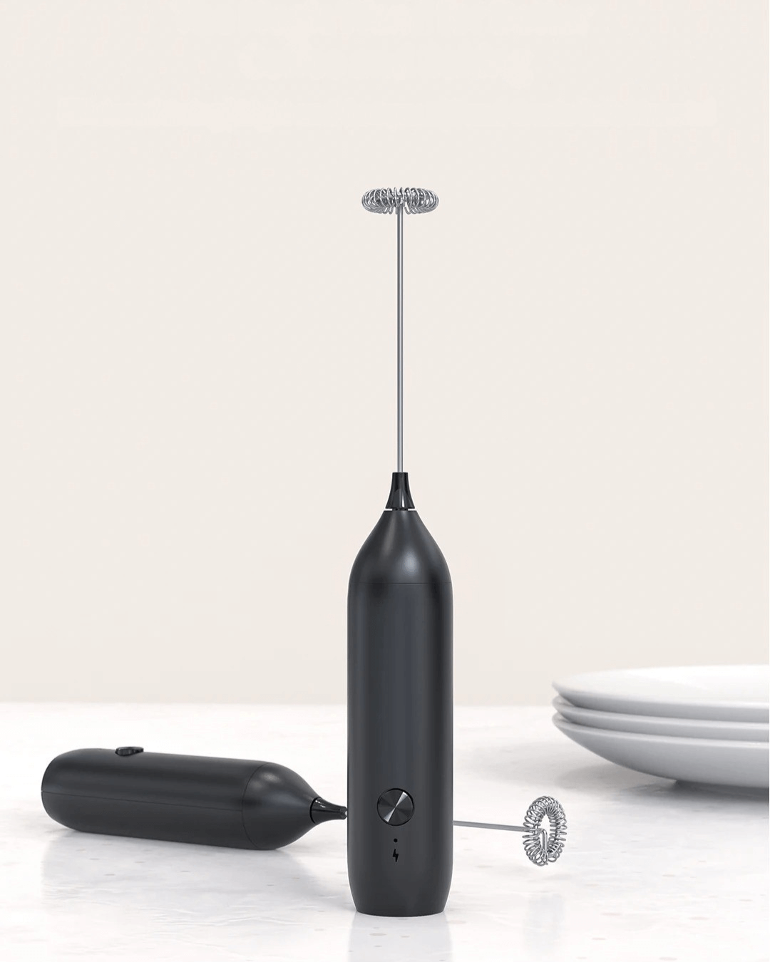 Black USB-C rechargeable matcha whisk and milk frother with stainless steel head on a counter.