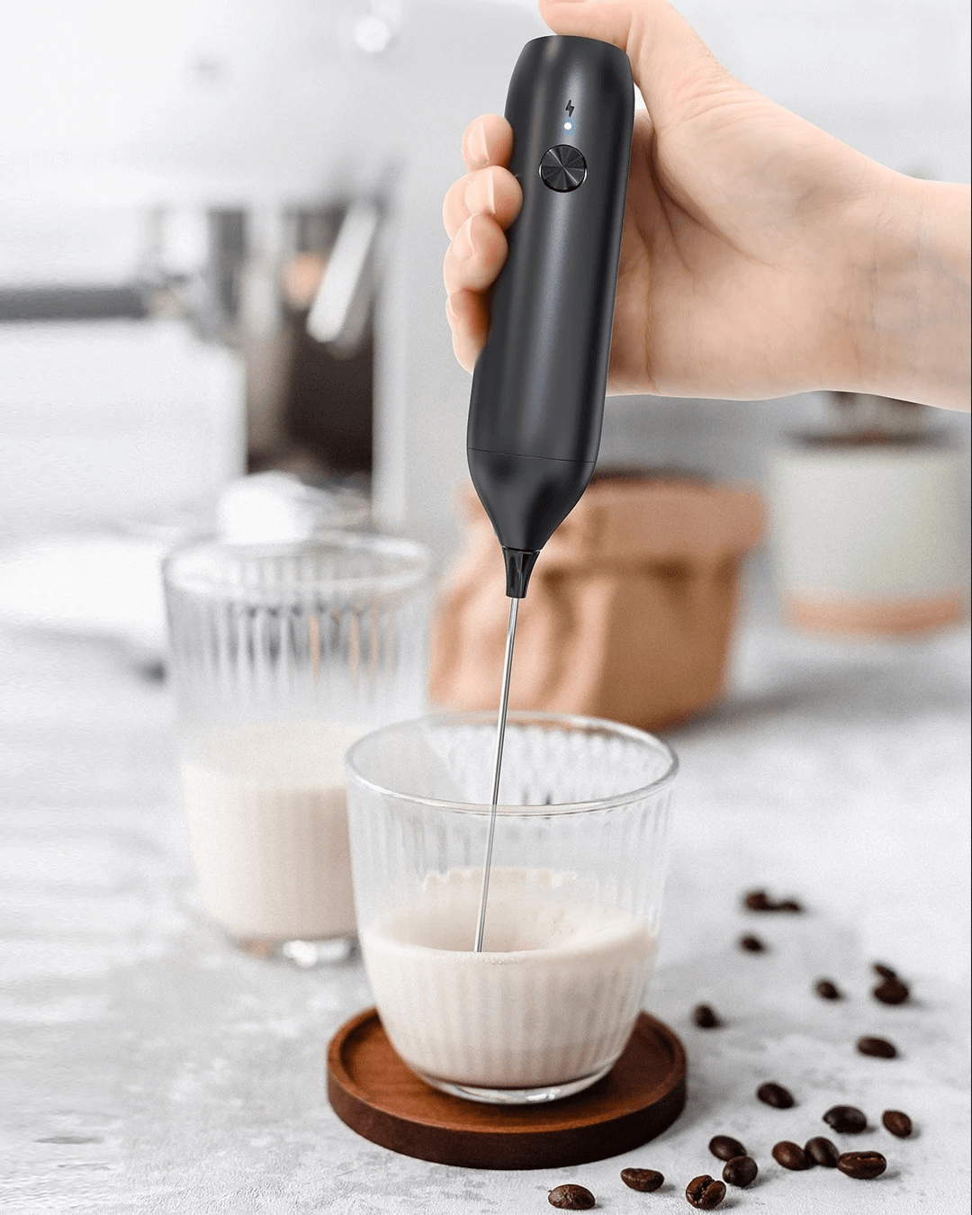 Handheld USB-C rechargeable milk frother in use, blending milk in a glass with coffee beans nearby.