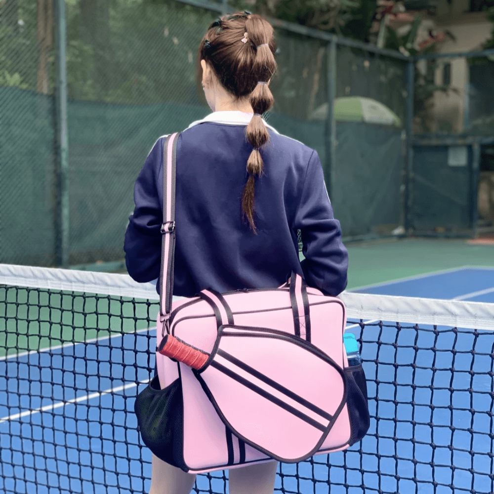 Woman carrying a pink waterproof padel racket bag with external sleeve, ready for a game on the court.