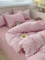 Cozy pink gingham bedding set with pillows and a teddy bear, perfect for a serene bedroom retreat.