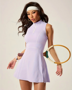 Female model wearing a lavender padel tennis dress with zip polo neck, built-in shorts, and holding a racket.