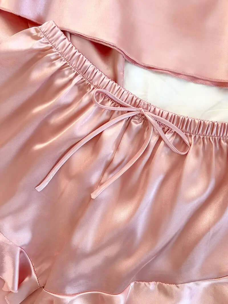 Close-up of women's soft satin pajama shorts featuring an elastic waistband and bow tie detail in light pink.