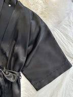 Close-up of a black satin kimono robe with a tie belt, part of a women's satin pajama set.