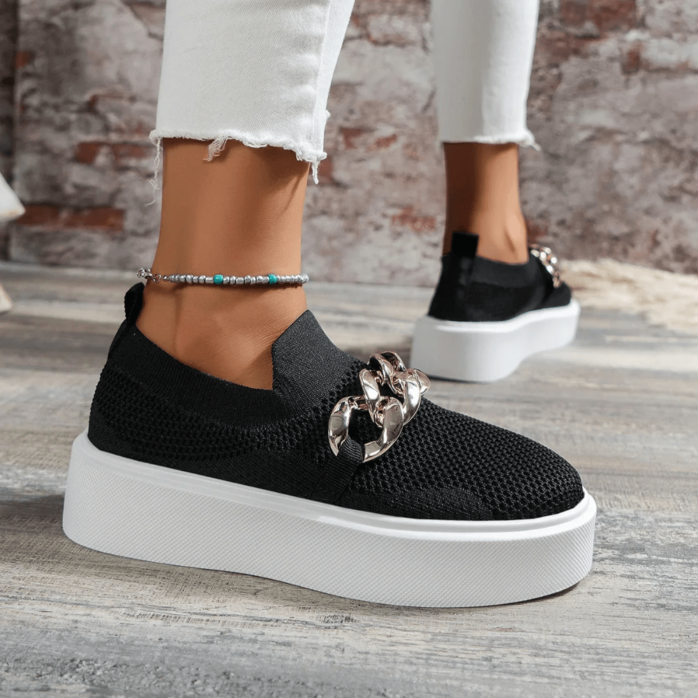 Stylish black women's slip-on shoes with chain detail and white platform sole, perfect for casual outings.