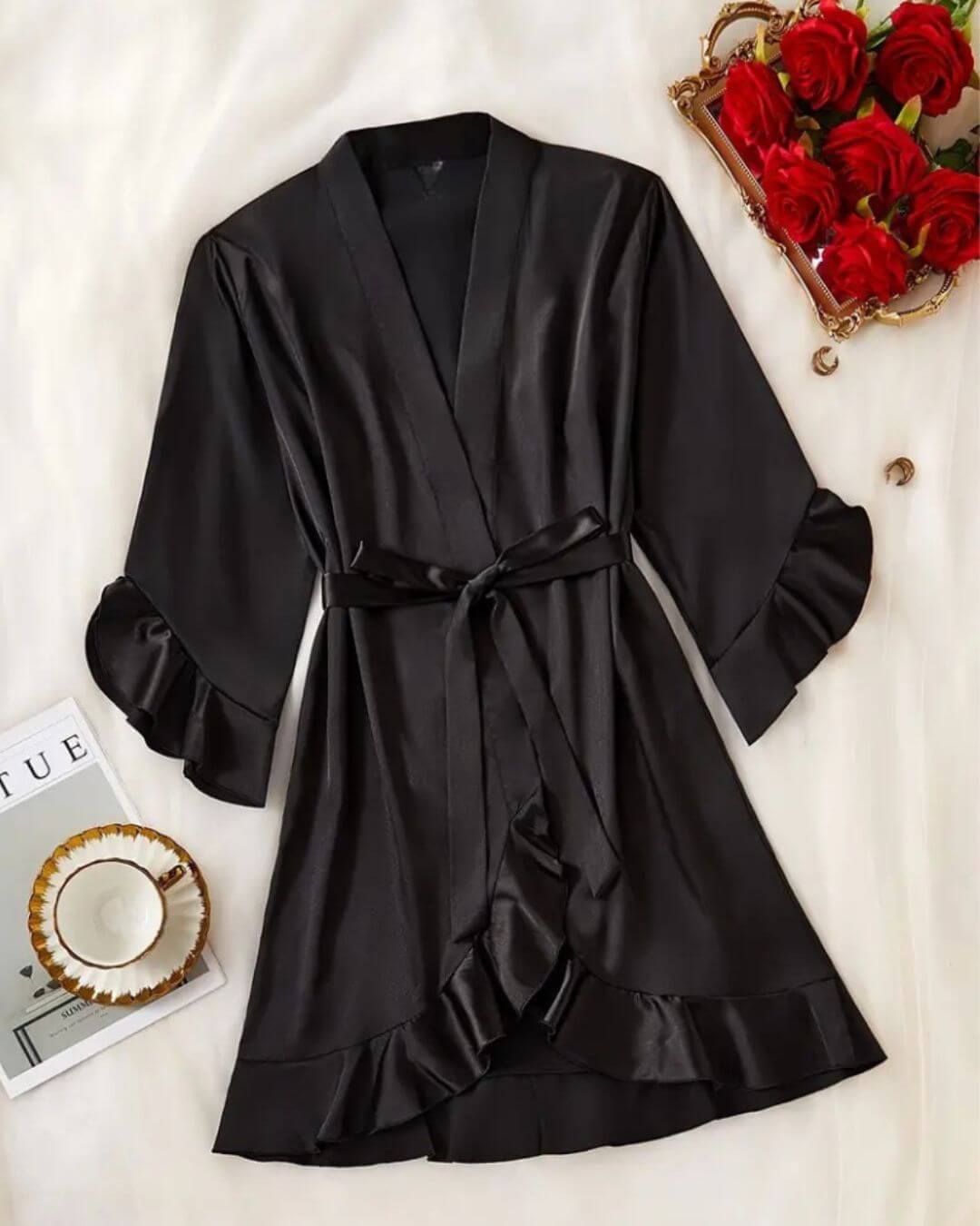 Black satin short dressing gown with ruffled sleeves and tie, styled with roses and accessories.