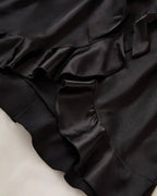 Close-up of the black satin fabric with ruffled hem of a women's luxury dressing gown.