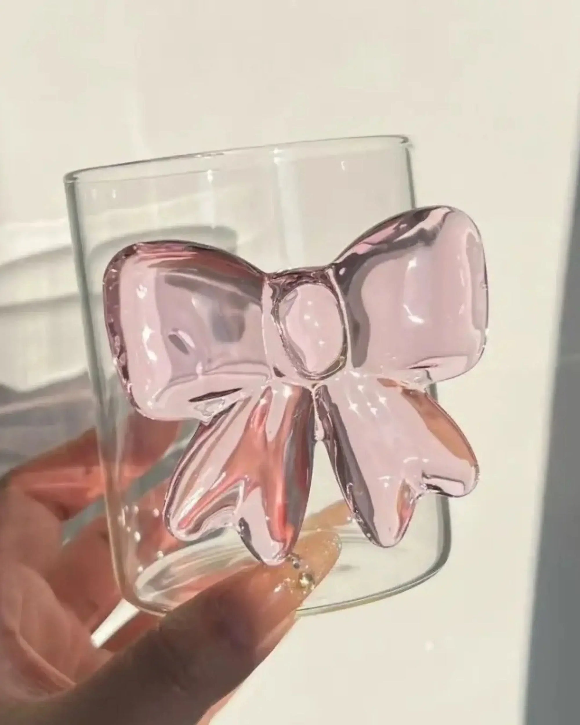 Pink bow glass cup held in hand with light reflection - aesthetic handmade drinking glass