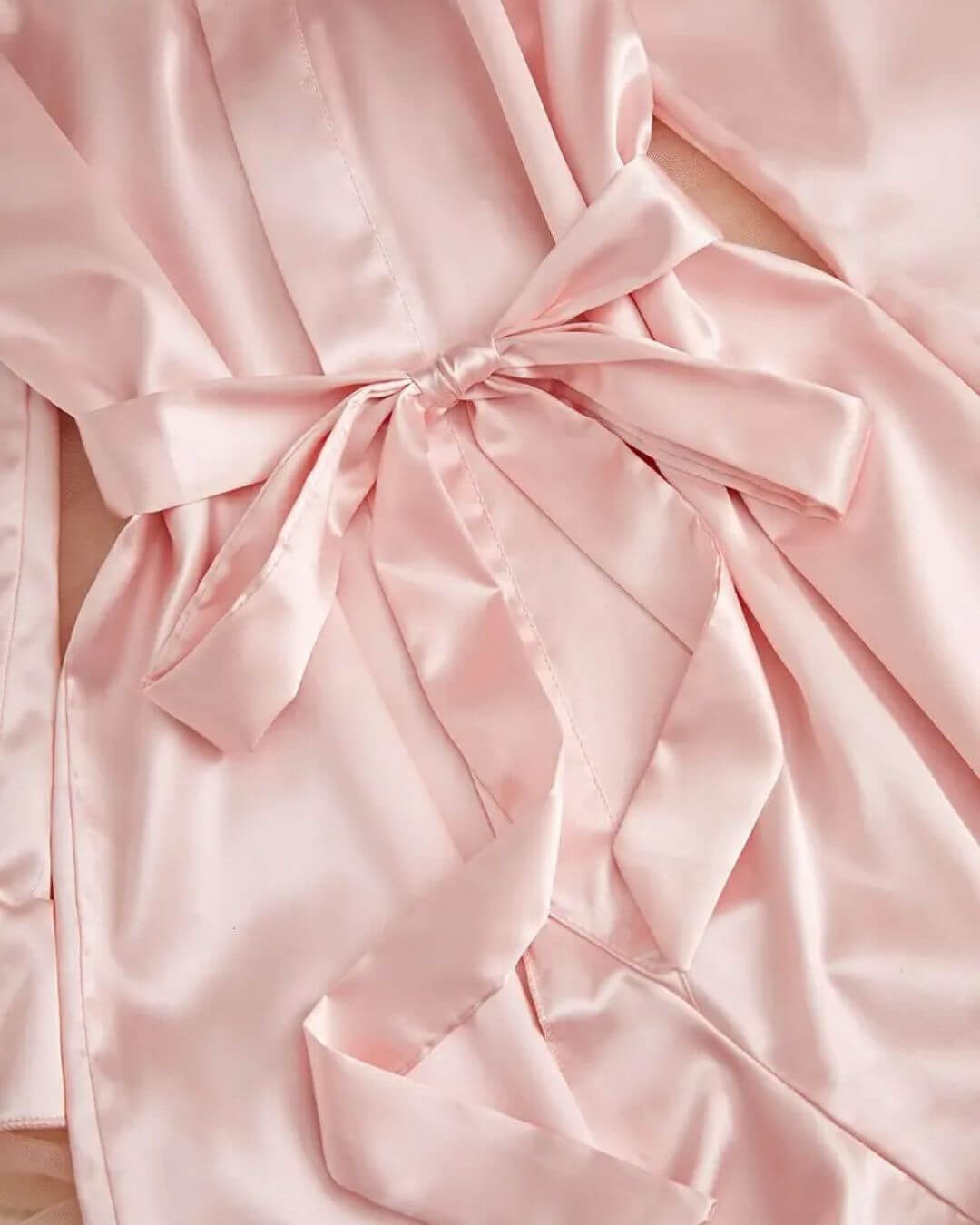 Close-up of a pink satin short dressing gown with a tied waist sash for a luxurious loungewear look.
